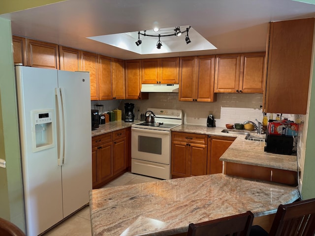 kitchen featuring white appliances, under cabinet range hood, brown cabinets, a sink, and light tile patterned floors