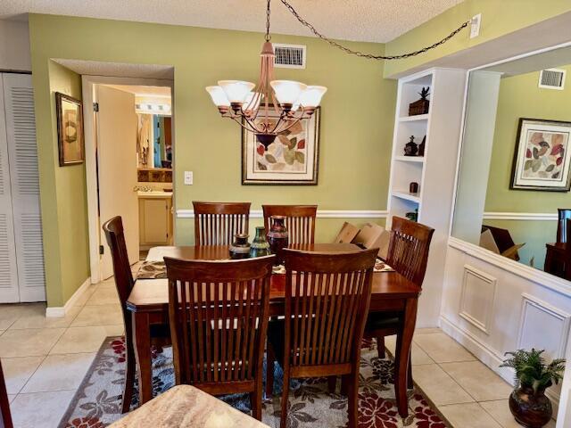 dining space with a textured ceiling, an inviting chandelier, light tile patterned floors, and visible vents