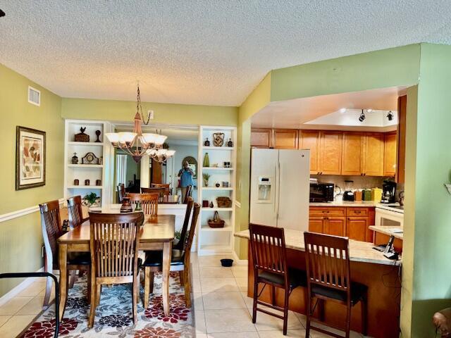dining area with light tile patterned floors, visible vents, a textured ceiling, and a chandelier