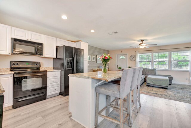 5810 Tucker Rd, Jupiter, FL 33458 - kitchen with black appliances, white cabinets, a ceiling fan, a breakfast bar, and light stone counters
