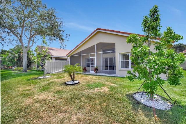 back of property with fence, a tile roof, stucco siding, a sunroom, and a yard