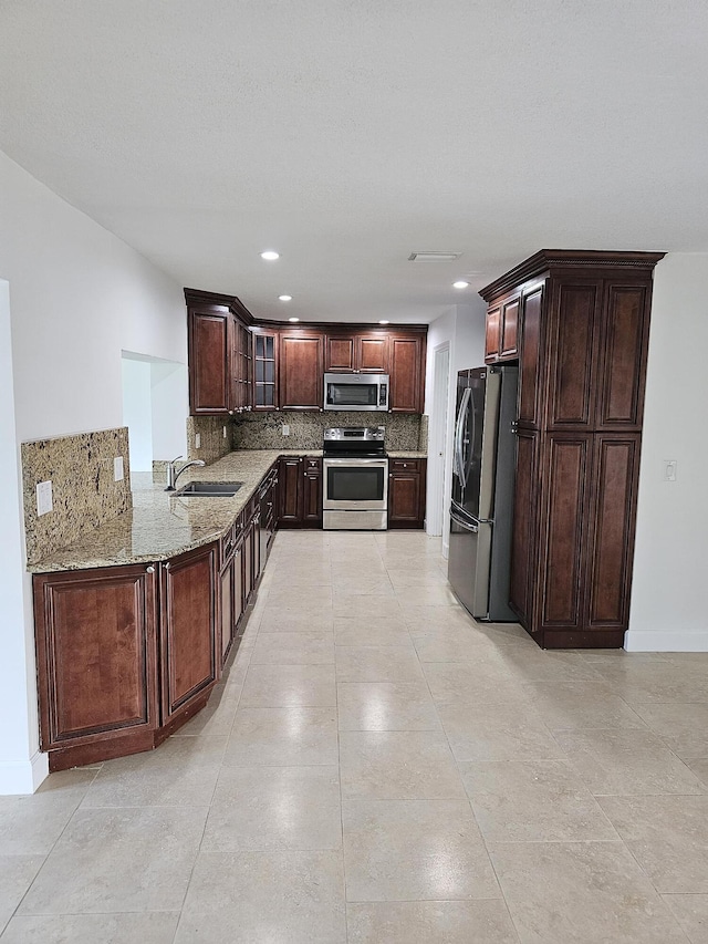 kitchen featuring light stone counters, a sink, appliances with stainless steel finishes, dark brown cabinetry, and backsplash