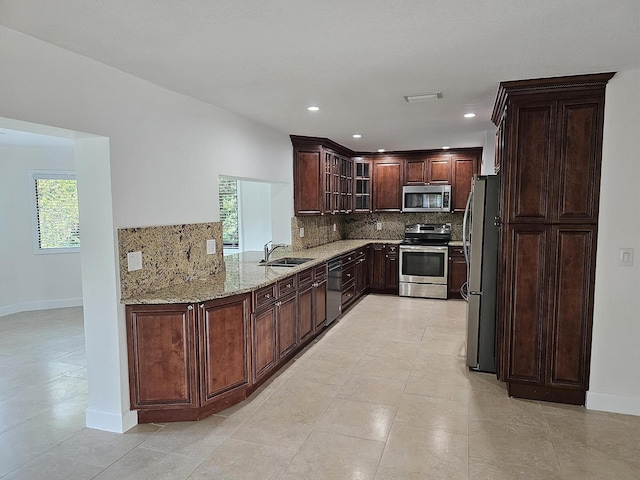 kitchen featuring dark brown cabinetry, light stone countertops, backsplash, and appliances with stainless steel finishes