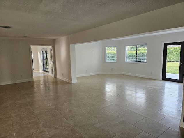 tiled spare room with a textured ceiling, a healthy amount of sunlight, visible vents, and baseboards