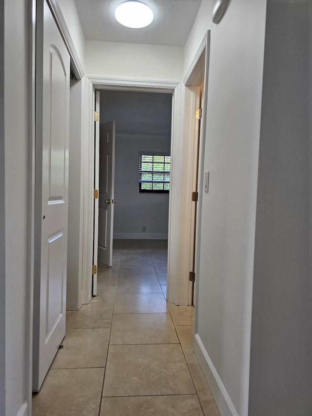 corridor featuring light tile patterned floors, a textured ceiling, and baseboards