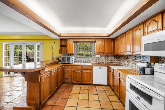 kitchen with brown cabinetry, white appliances, a peninsula, and decorative backsplash