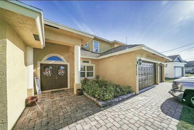 doorway to property with decorative driveway, a garage, and stucco siding