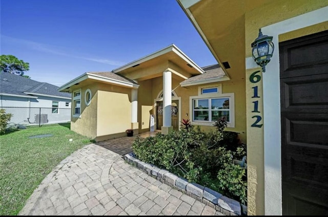 entrance to property featuring a yard, stucco siding, and fence
