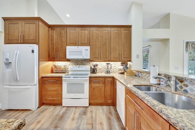 kitchen featuring light wood finished floors, light stone countertops, a sink, backsplash, and white appliances