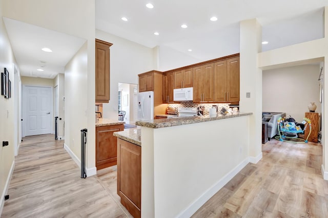 kitchen featuring light stone countertops, white appliances, decorative backsplash, brown cabinetry, and light wood finished floors