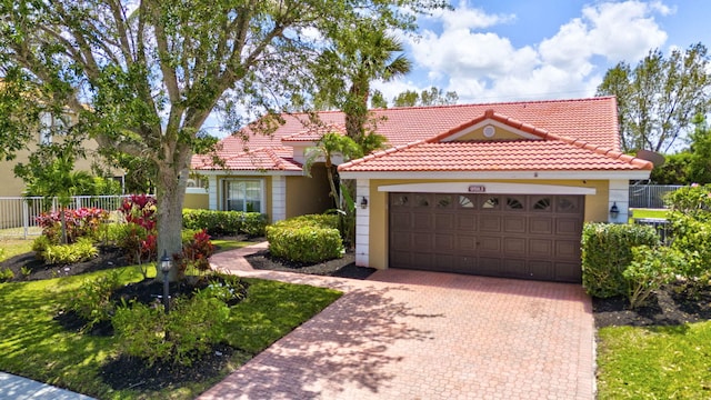 mediterranean / spanish house featuring a garage, fence, stucco siding, and a tiled roof