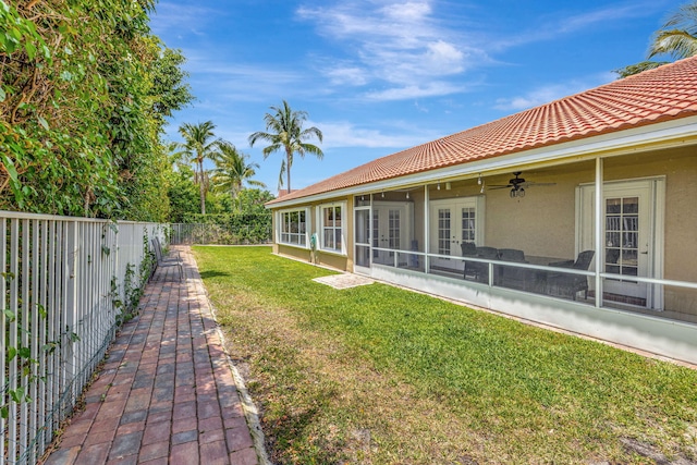 view of yard featuring french doors, a fenced backyard, a ceiling fan, and a sunroom