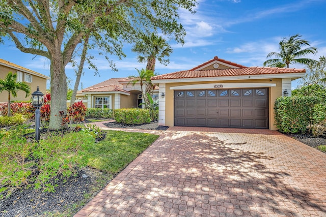 mediterranean / spanish-style home featuring a garage, a tile roof, stucco siding, and decorative driveway
