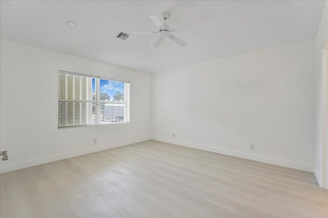 empty room with ceiling fan, visible vents, baseboards, and light wood finished floors
