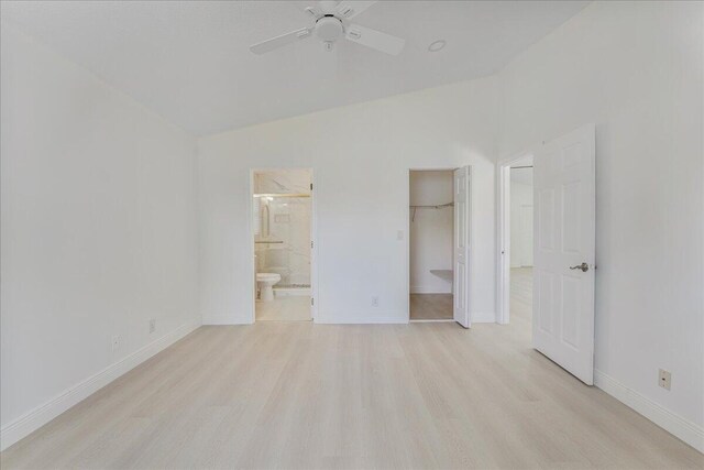 unfurnished bedroom featuring ceiling fan, a walk in closet, ensuite bath, baseboards, and light wood-type flooring