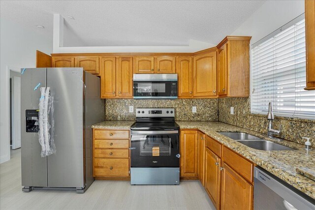 kitchen with brown cabinetry, backsplash, a sink, light stone counters, and stainless steel appliances