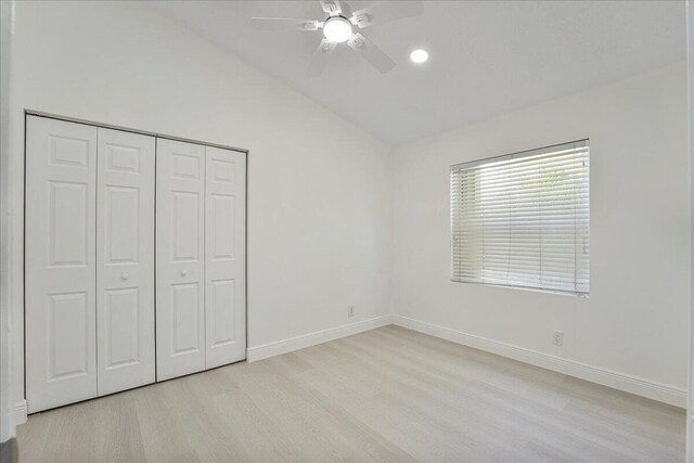 unfurnished bedroom featuring light wood-style floors, baseboards, vaulted ceiling, and a closet