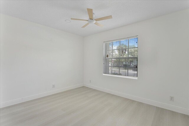 empty room with a ceiling fan, a textured ceiling, baseboards, and light wood-style floors