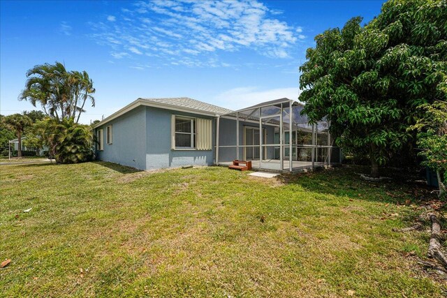 rear view of property with a lawn, glass enclosure, and stucco siding