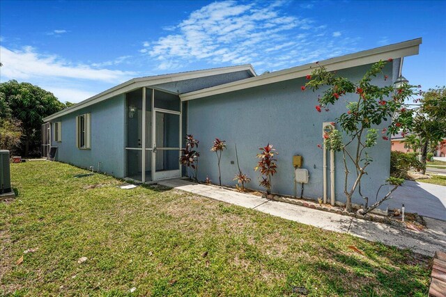 view of side of property with a lawn, central AC unit, stucco siding, and a sunroom