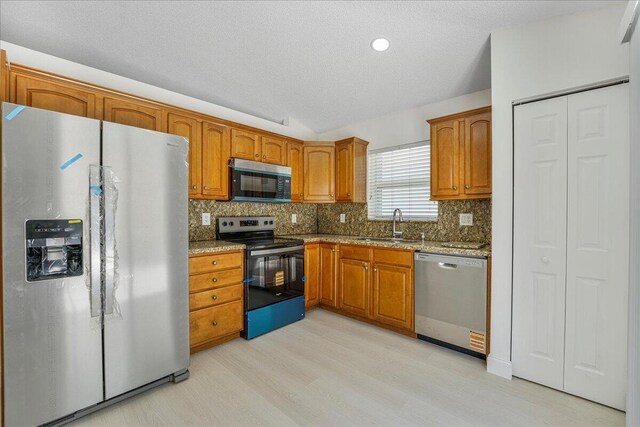 kitchen with brown cabinetry, decorative backsplash, light wood-type flooring, a textured ceiling, and stainless steel appliances
