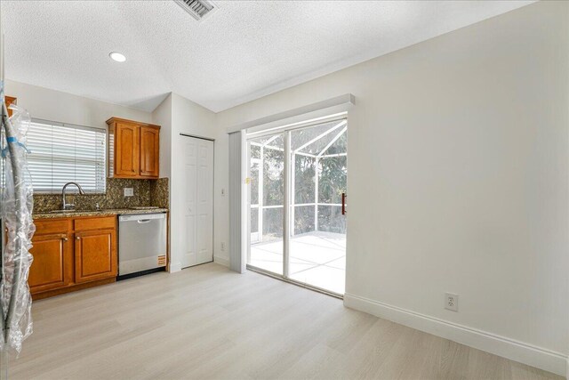 kitchen with brown cabinetry, dishwasher, a sink, dark stone countertops, and light wood finished floors