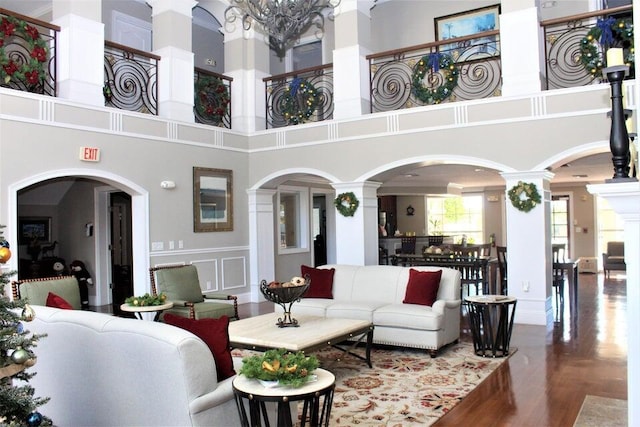 living room featuring a high ceiling, wood finished floors, decorative columns, and a decorative wall
