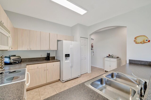 kitchen featuring a sink, light brown cabinets, white appliances, arched walkways, and light tile patterned floors