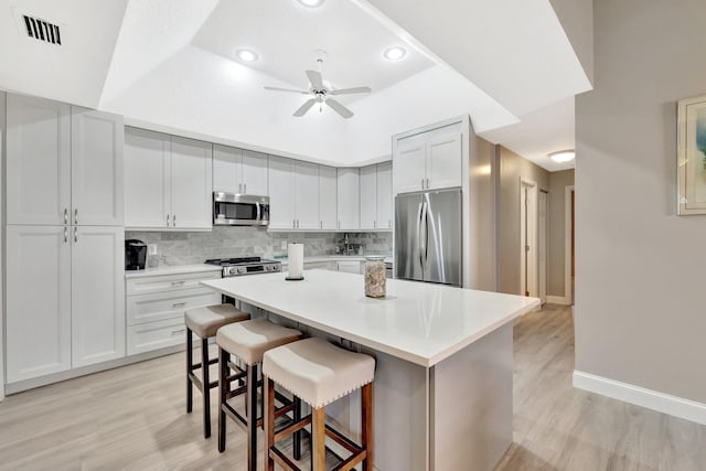 kitchen with light wood-style floors, a kitchen breakfast bar, stainless steel appliances, a kitchen island, and visible vents