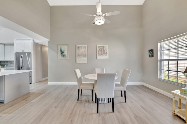 dining room featuring light wood-type flooring, a ceiling fan, baseboards, and high vaulted ceiling