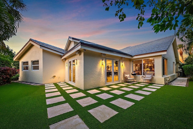 back of house at dusk with a lawn, stucco siding, and a patio