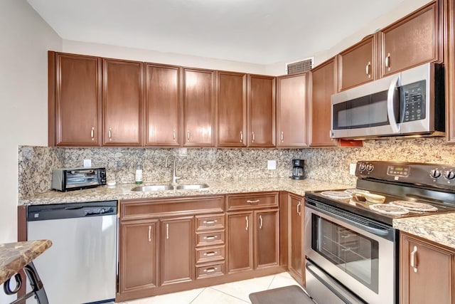 4049 Wolverton C, Boca Raton, FL 33434 - kitchen featuring appliances with stainless steel finishes, tasteful backsplash, light tile patterned floors, brown cabinets, and light stone countertops