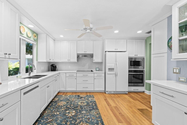 kitchen with a sink, stainless steel appliances, white cabinetry, light wood-type flooring, and under cabinet range hood