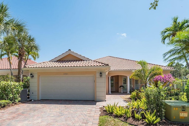 3352 SE Cascadia Way, Hobe Sound, FL 33455 - mediterranean / spanish-style house with driveway, a tile roof, a garage, cooling unit, and stucco siding