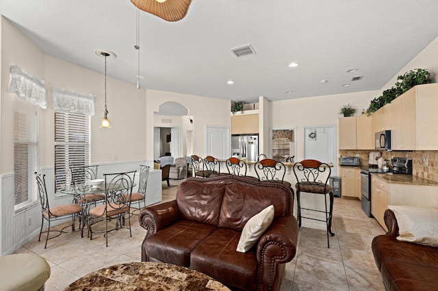 living area with a wainscoted wall, visible vents, a toaster, arched walkways, and light tile patterned floors