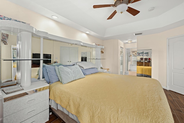 bedroom with a tray ceiling, visible vents, dark wood-style flooring, ceiling fan, and recessed lighting