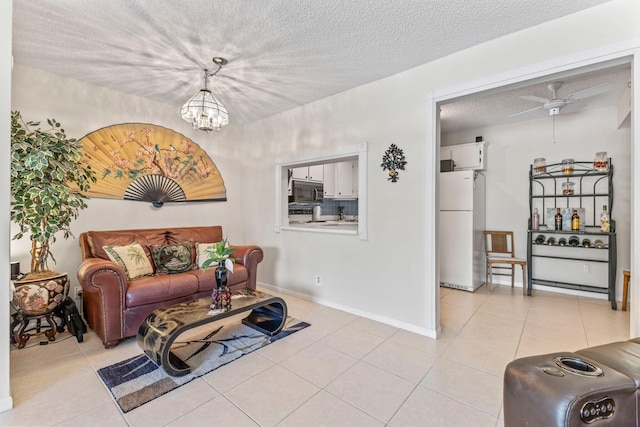 living area with light tile patterned floors, baseboards, ceiling fan with notable chandelier, and a textured ceiling