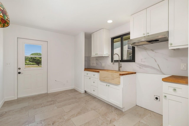 kitchen featuring under cabinet range hood, a sink, wood counters, backsplash, and recessed lighting