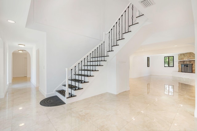 staircase with arched walkways, baseboards, marble finish flooring, a high ceiling, and a fireplace