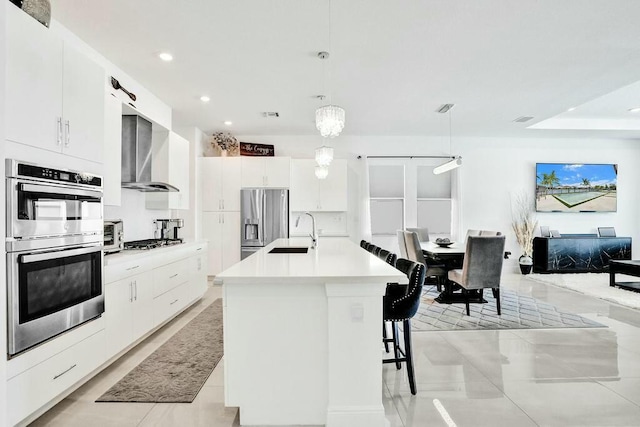 12170 N Baypoint Cir, Parkland, FL 33076 - kitchen featuring a sink, a center island with sink, white cabinetry, wall chimney range hood, and appliances with stainless steel finishes