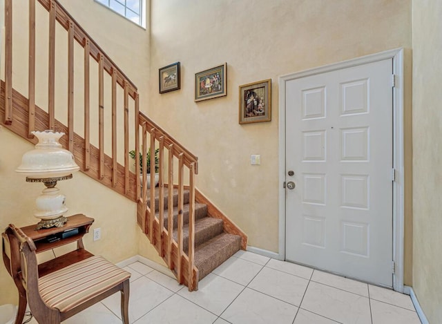 foyer entrance featuring stairs, baseboards, light tile patterned floors, and a high ceiling