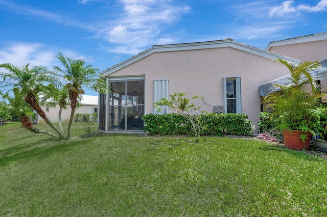 back of house featuring stucco siding, a lawn, and a sunroom