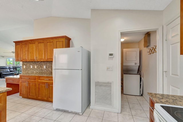 kitchen with freestanding refrigerator, brown cabinetry, light tile patterned floors, visible vents, and stacked washer and clothes dryer