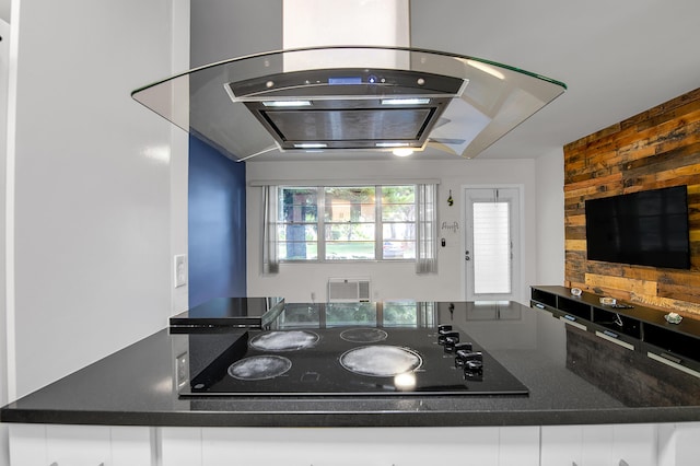 kitchen with wooden walls, dark countertops, island exhaust hood, and black electric stovetop