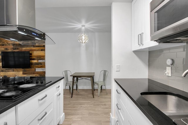 kitchen featuring stainless steel microwave, a sink, island range hood, black electric cooktop, and backsplash