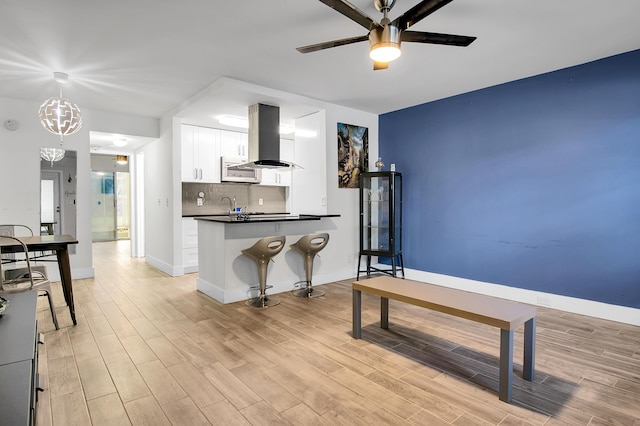 kitchen featuring decorative backsplash, white cabinets, island range hood, dark countertops, and ceiling fan with notable chandelier