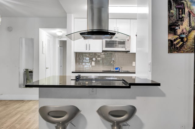 kitchen featuring a kitchen breakfast bar, a sink, dark countertops, black electric cooktop, and island exhaust hood