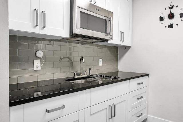 kitchen featuring stainless steel microwave, a sink, tasteful backsplash, dark countertops, and white cabinets