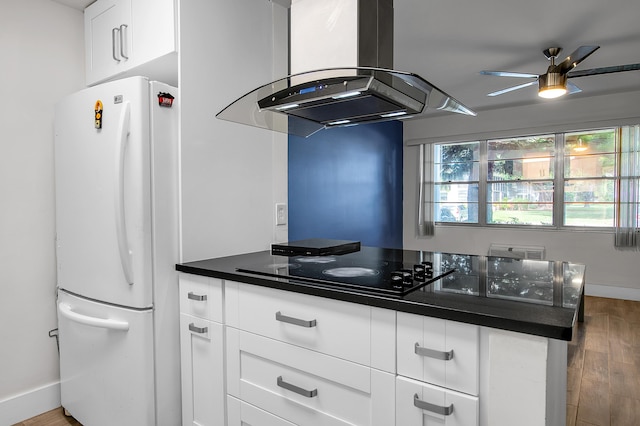 kitchen featuring black electric cooktop, a ceiling fan, island range hood, freestanding refrigerator, and wood finished floors