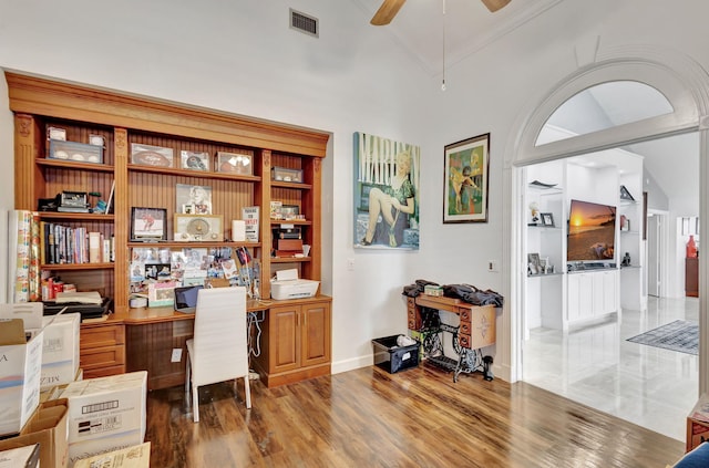 office space featuring ceiling fan, visible vents, crown molding, built in desk, and wood finished floors